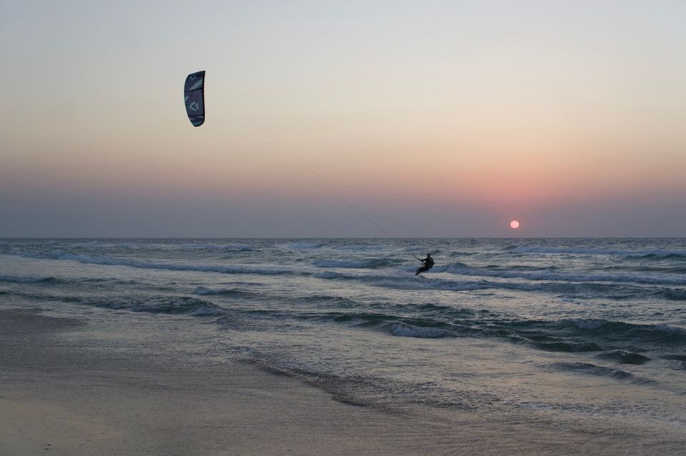 Un rider en kitesurf au coucher du soleil, aile à gauche et soleil à l'horizon à droite.