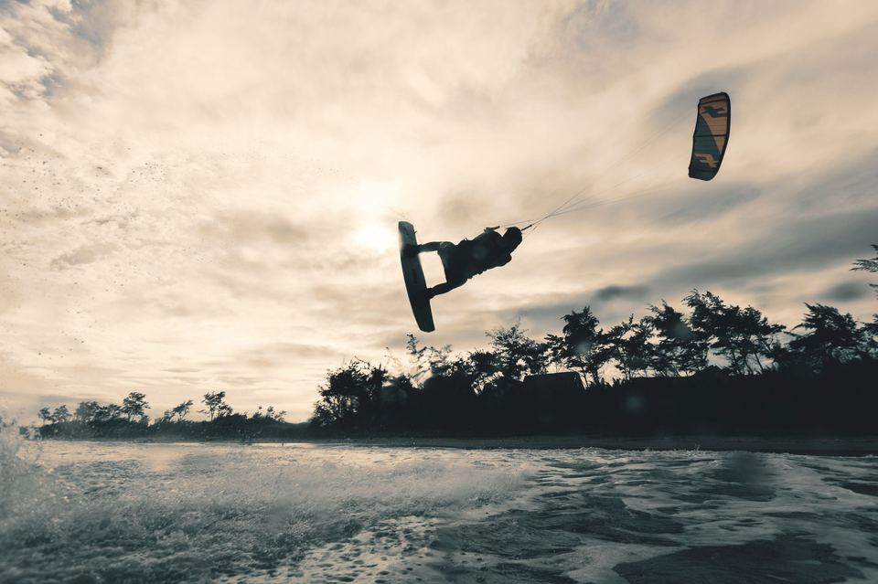 Un rider effectue un saut en kitesurf à contre-jour, au coucher du soleil.